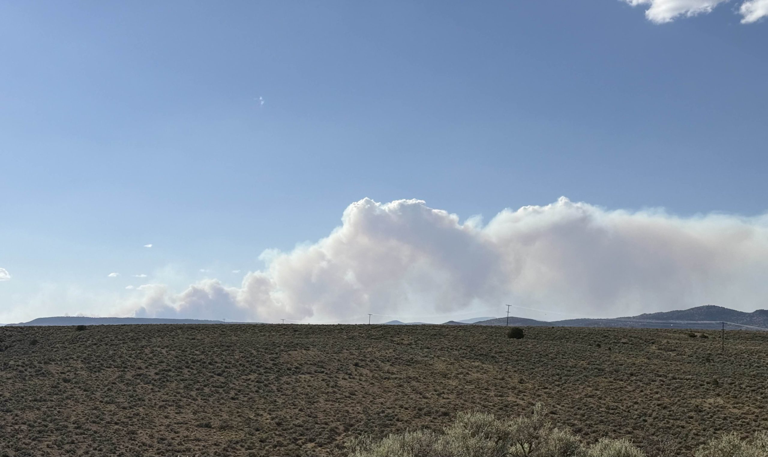 A wildfire smoke plume rising over a sagebrush plateau in northern New Mexico